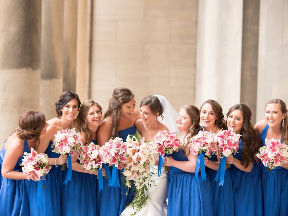 A group of bridesmaids in blue dresses surrounding a bride.