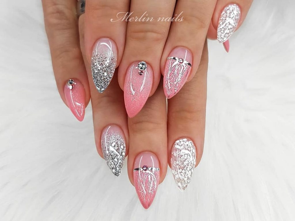 Pink colored wedding nails paired with white accent artwork. The nails also have jewel accents on a medium length pointed nail.