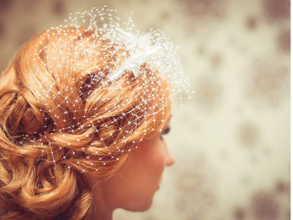 Red haired woman facing sideways with soft curled hair and a white fishnet veil.