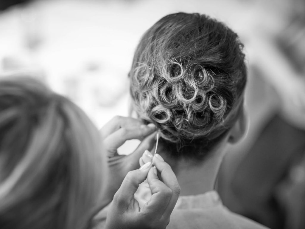 Black and white photo of a woman getting her hair styled in a tight loop updo.