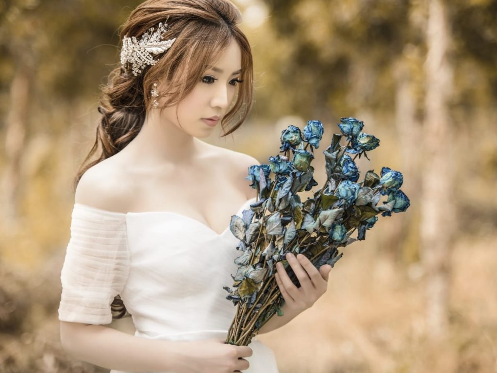 Woman holding a bouquet of flowers in a wedding dress modeling a spiral ponytail with bangs hairstyle.  