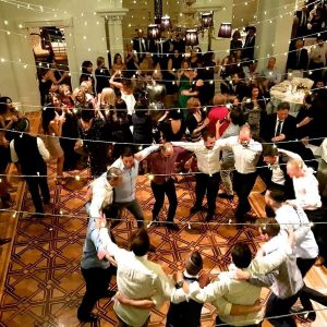 Group of men holding arms in a circle and dancing on the dance floor at a wedding reception