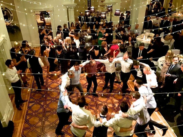 Group of men holding arms in a circle and dancing on the dance floor at a wedding reception