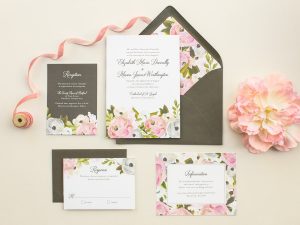 Flat lay display of a wedding invitation with white, black and pink flower accents