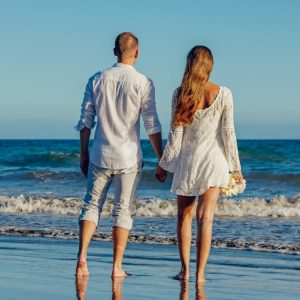 Couple walking on the seashore with beach wedding attire and barefoot