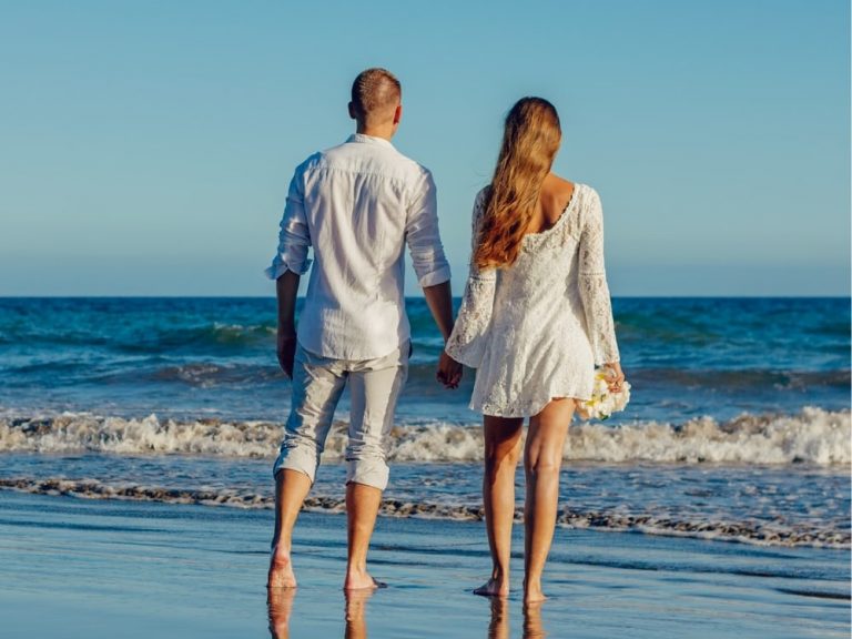 Couple walking on the seashore with beach wedding attire and barefoot