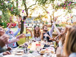 A couple dining outdoors with guests at the table and throwing confetti as wedding entertainment