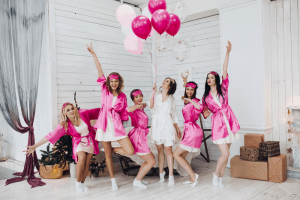 Girls posing wearing pink bathrobes and bride at the center wearing a white bathrobe holding balloons