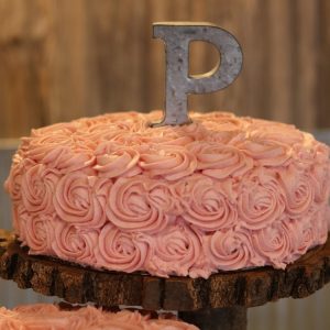 A pink champagne cake with a letter P cake topper made of metal.