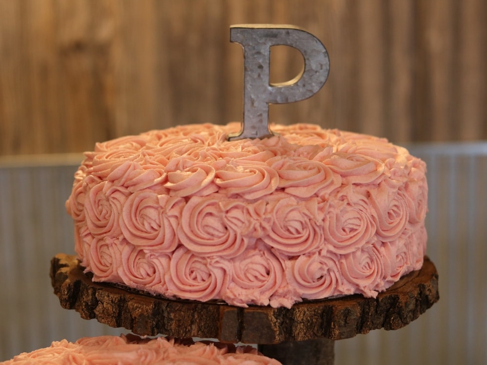 A pink champagne cake with a letter P cake topper made of metal. 