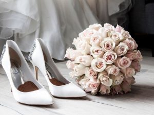 Bridal shoes sitting on the floor next to a bouquet of flowers.